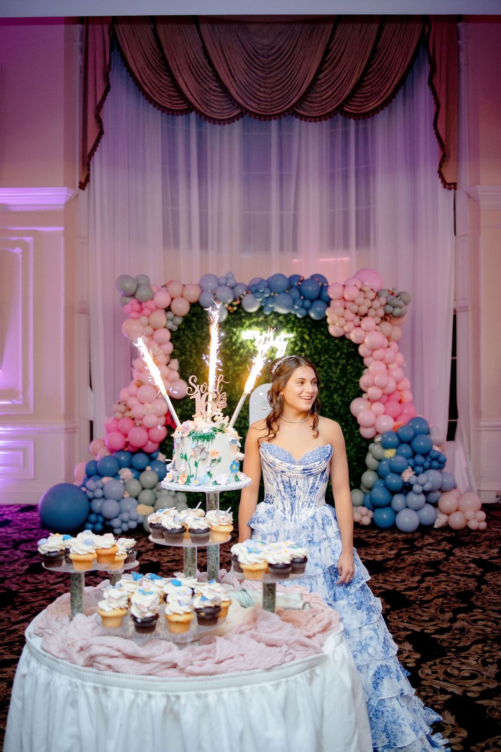 A gender reveal party table decorated with pink and blue balloon garlands and tiered cakes with sparklers on top.