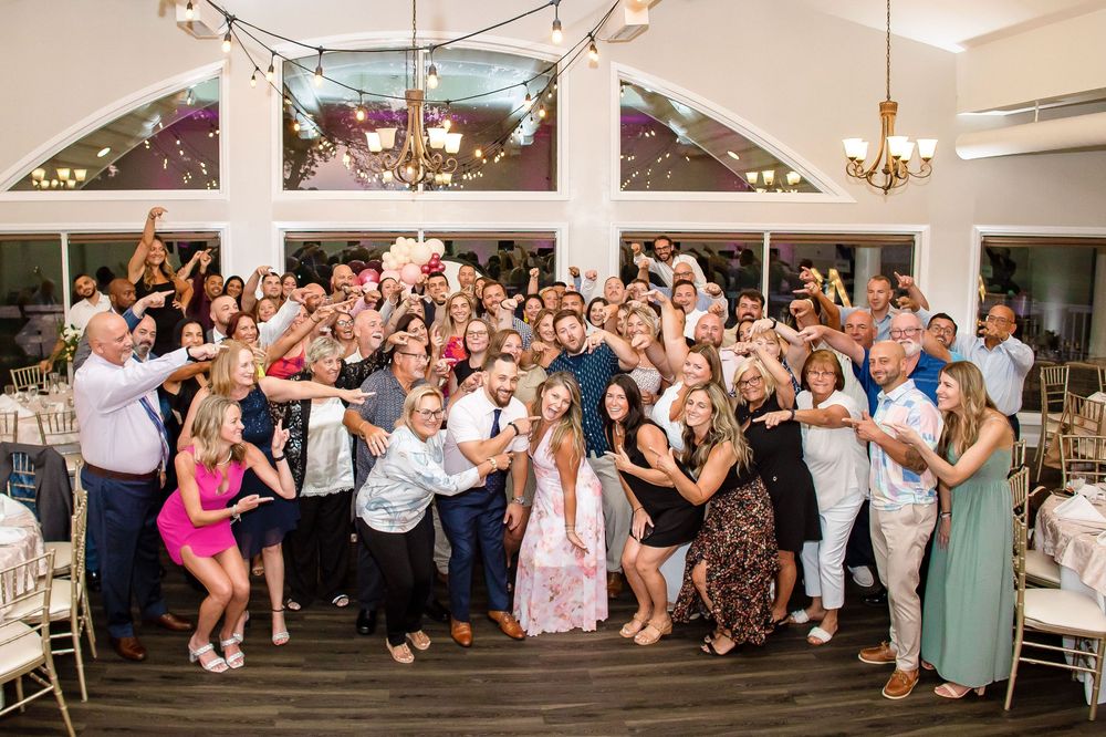 Large group of wedding guests celebrating and posing together for a photo inside a reception venue with white pillars.