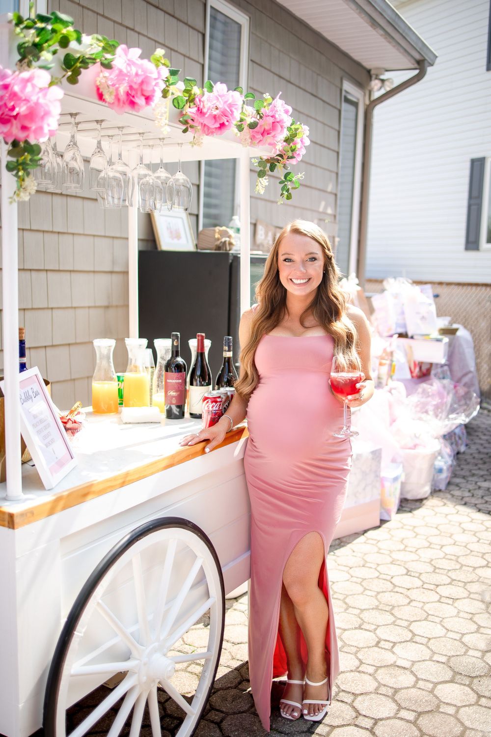 A decorated beverage cart with pink floral arrangements and refreshments at an outdoor party.