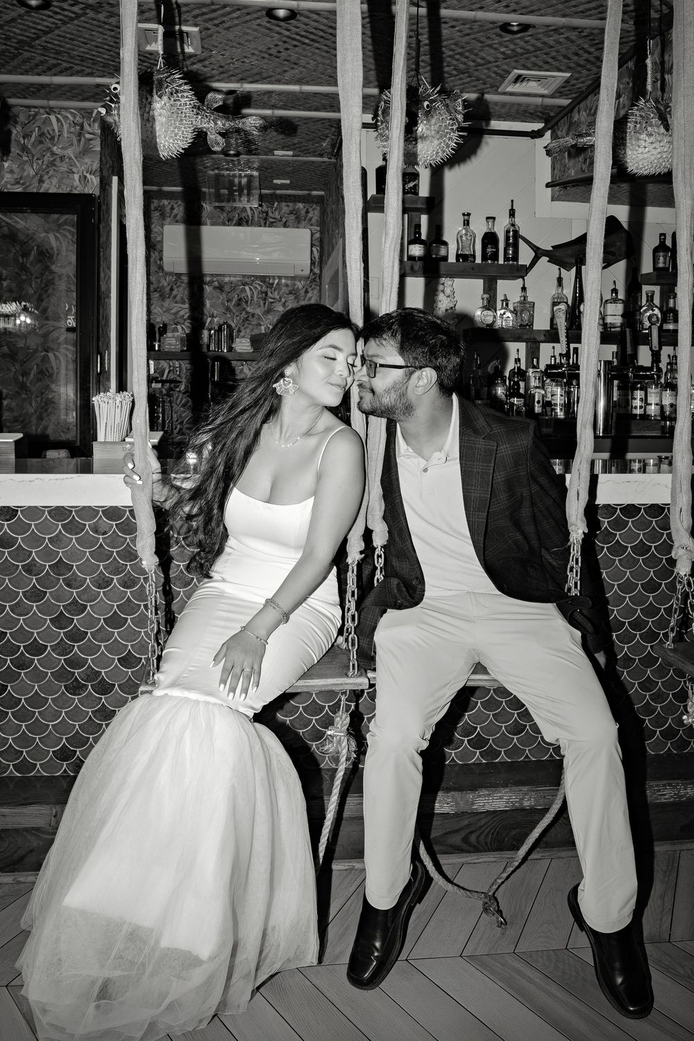 Black and white photo of a bride and groom sharing a romantic kiss on swings inside an elegant bar.