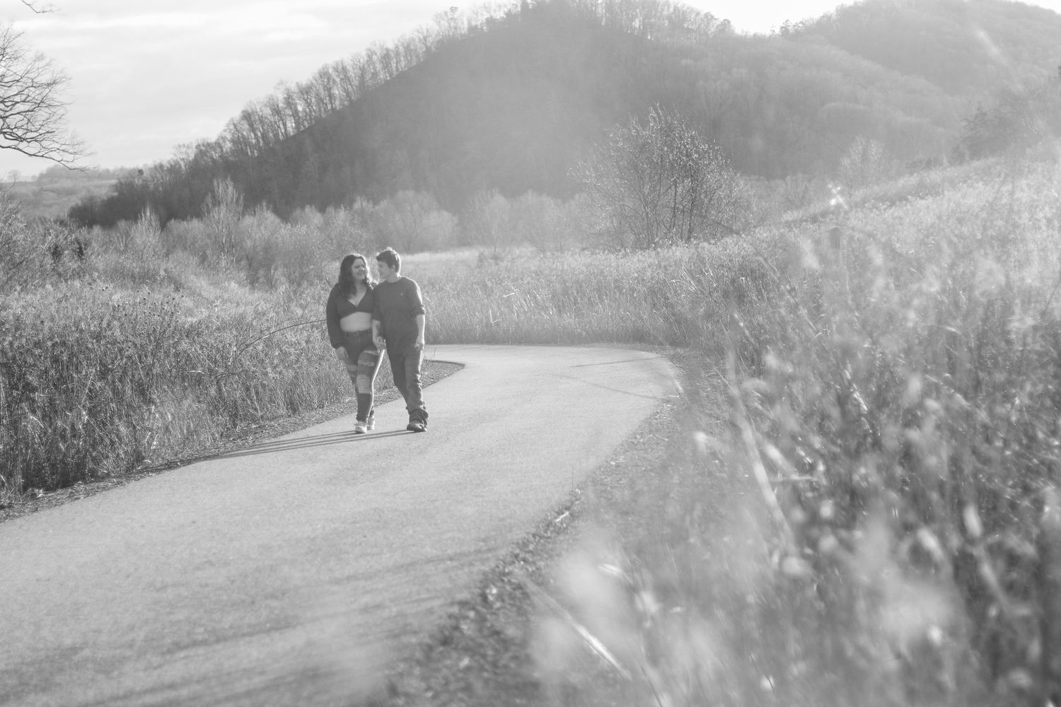 Black and white image of two people walking together on a misty rural road.