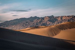 Golden sand dunes with rippled texture against a mountain range at sunset in Death Valley.
