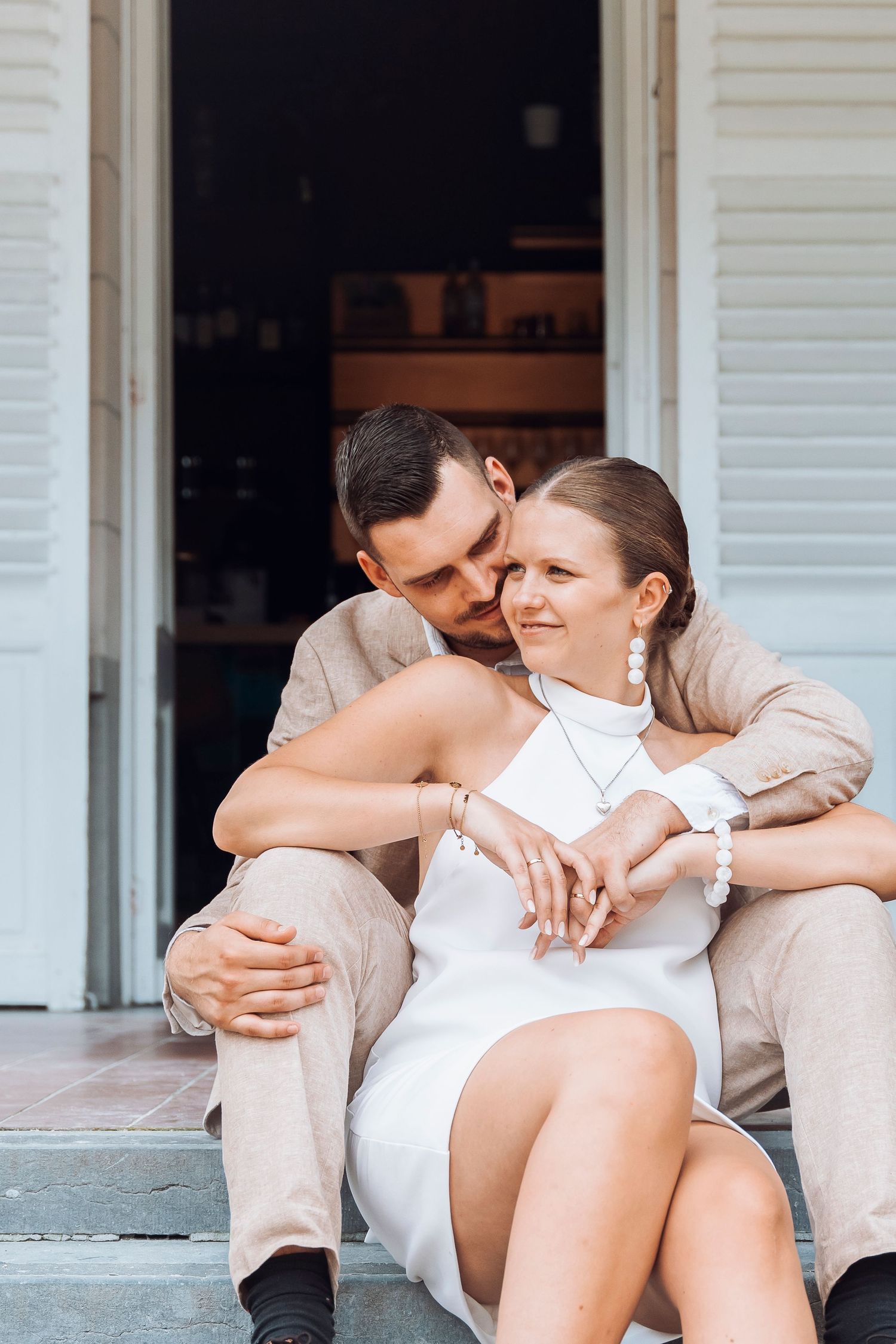 Couple in formal attire sharing an intimate moment on steps with white shutters.