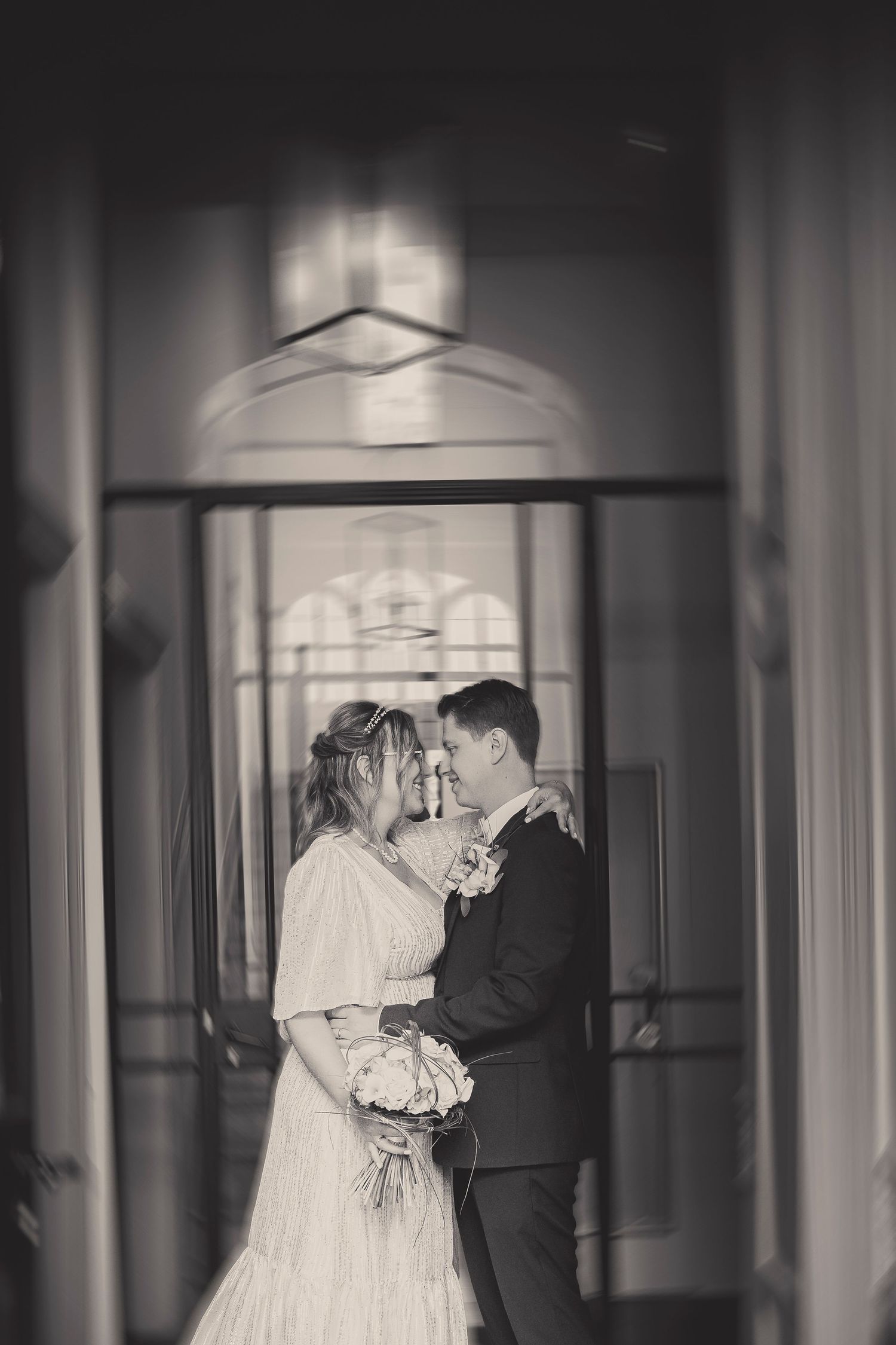 A dramatic black and white wedding portrait framed through a doorway with architectural details.