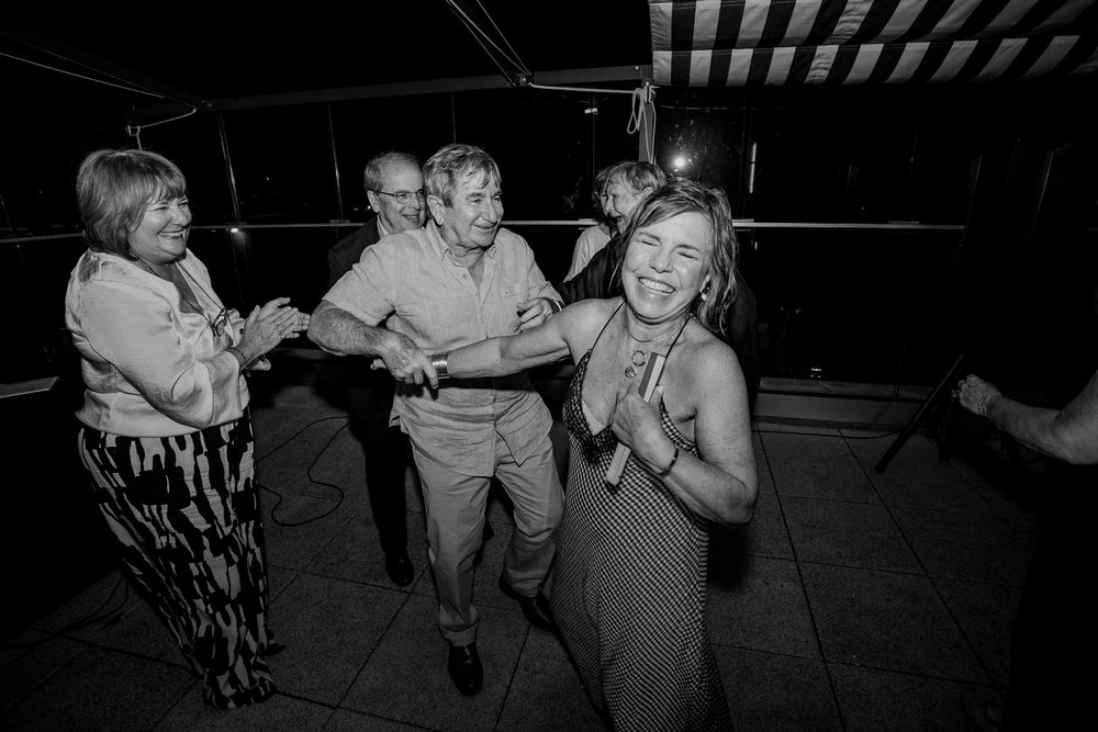 Black and white photo of joyful guests dancing at a wedding reception party outdoors at night.
