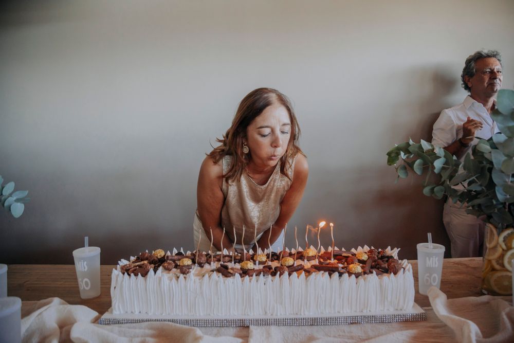 Young woman blowing out candles on a large birthday cake at a celebration party indoors.