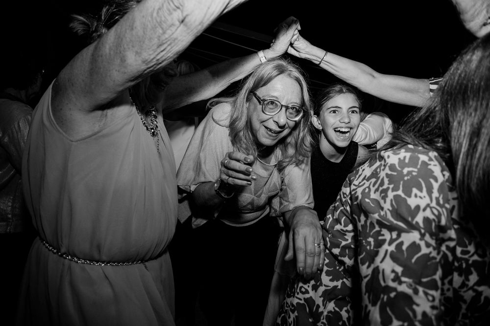 Black and white photo of women laughing and dancing together at a celebration, arms raised joyfully.