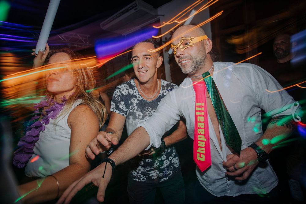 Three friends dancing and celebrating at a vibrant nightclub party with colorful lights.