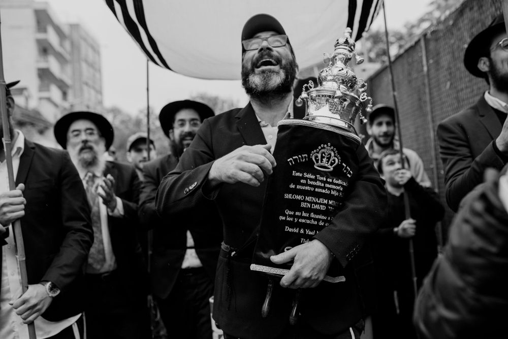 A man in a black shirt holds up a bottle while celebrating with others wearing hats.