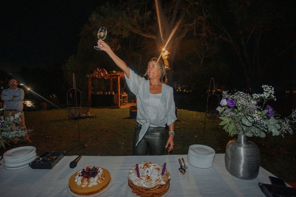 Woman raising a wine glass in a toast at an outdoor night celebration with cakes on the table.