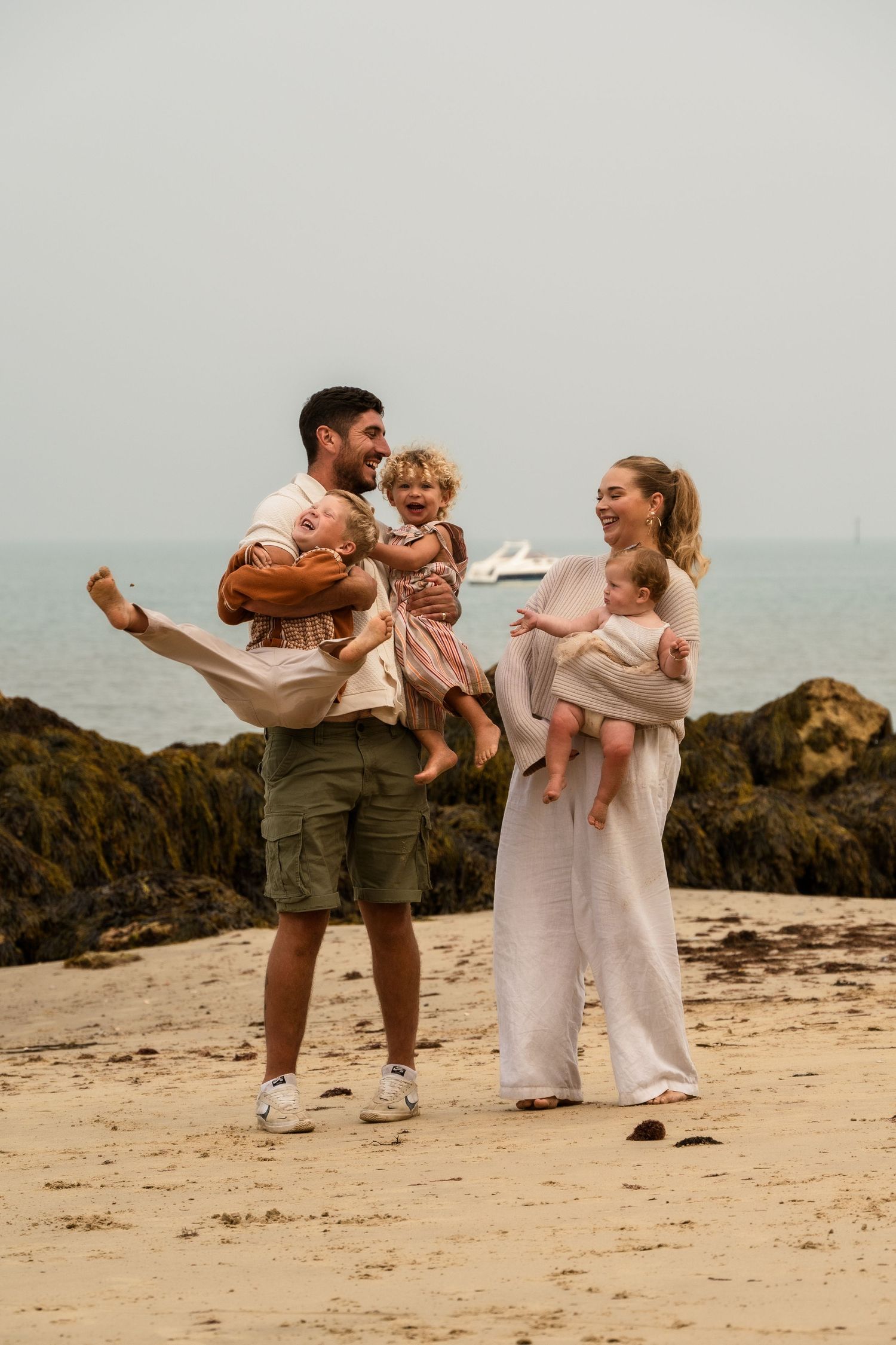 Family enjoying playful moments together on a rocky beach during sunset.
