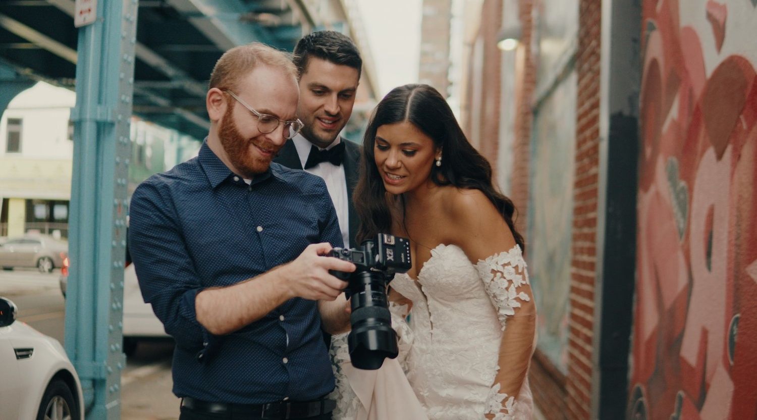 Photographer Zach Blum from Philadelphia shows wedding shots to a joyful couple under urban street art and steel beams. aka Zach Blub