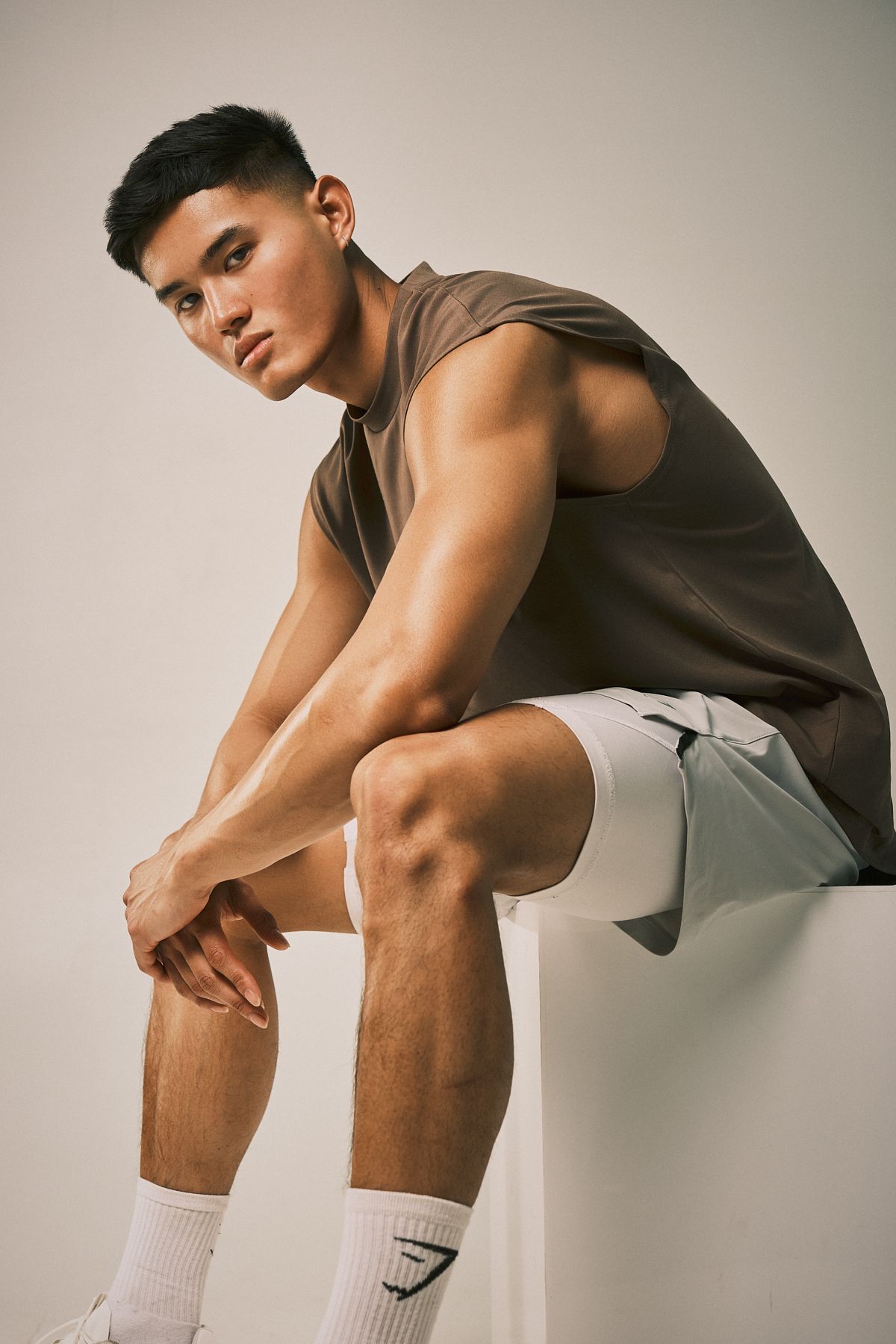Male model sitting with a serious expression, wearing a loose sleeveless top and shorts