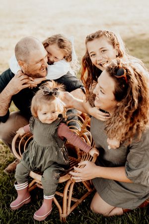 Happy family sitting together outdoors in a field sharing joyful laughter while gathering around a wicker chair.