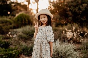 Child in floral dress standing in garden during golden hour.
