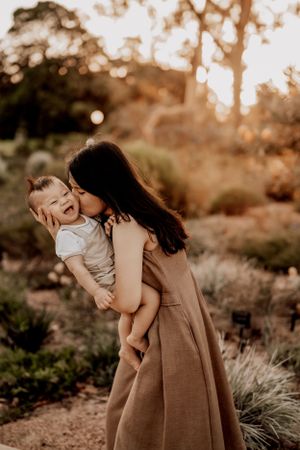 Parent and child share a joyful moment together outdoors at sunset in a natural garden setting.