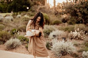 A figure in a flowing beige dress stands in a desert garden setting during golden hour.