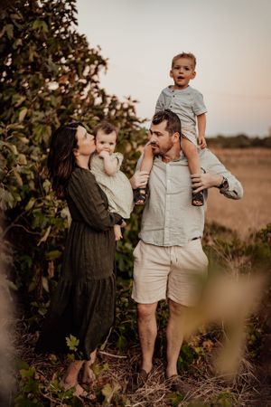 Family of four poses together among fruit trees at golden hour.