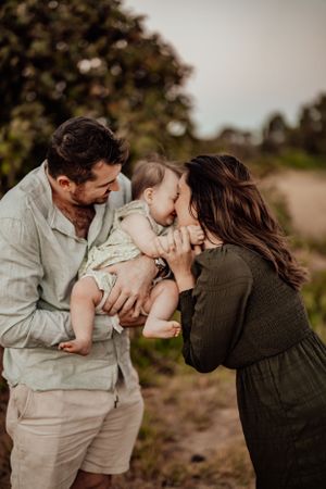 Parents share tender moment with baby during outdoor family photo session.