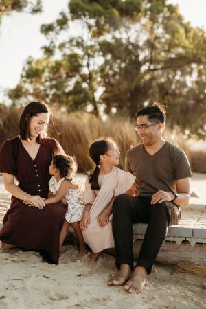 Family sitting together on sandy beach during golden hour sunset.