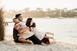 Romantic couple relaxing together on sandy beach at sunset with golden light and calm waters in background.