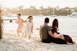 Family enjoying a sunset moment together on a sandy beach with children playing in the warm golden light.