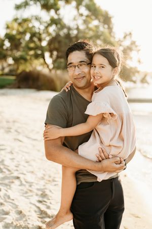 A loving couple shares a romantic embrace on a sandy beach at sunset, with warm golden light illuminating the scene.