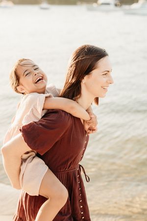 Two people share a joyful moment at the beach, with one giving a piggyback ride while wearing a burgundy dress.