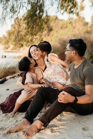 Family lying together on sandy beach beneath trees during golden hour.