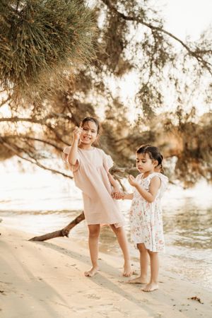 Family playing and dancing together on sandy beach under overhanging trees.