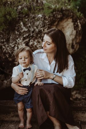 Sweet candid moment between parent and child sitting together in coordinated white and brown outfits against dark background.