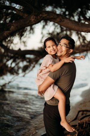 Parents sharing joyful moments with child at sunset on tropical beach.
