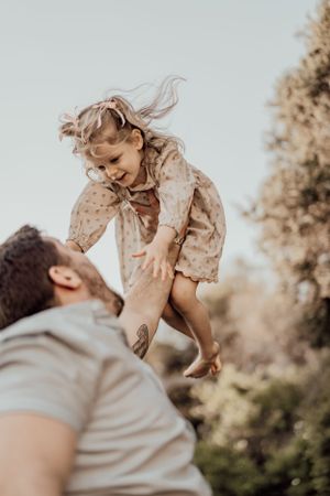 Parent lifts laughing child high in the air during sunset portrait session.