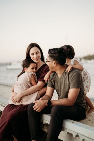 Family sharing intimate moments together while sitting on beach at sunset.