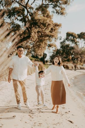 A family wearing coordinated white and brown outfits plays together on a sandy beach during golden hour.