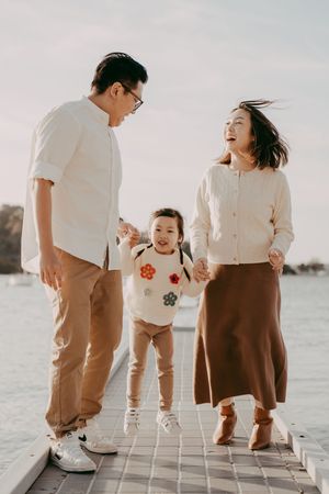 Family in coordinating brown and white outfits poses together on a dock at sunset by the water.