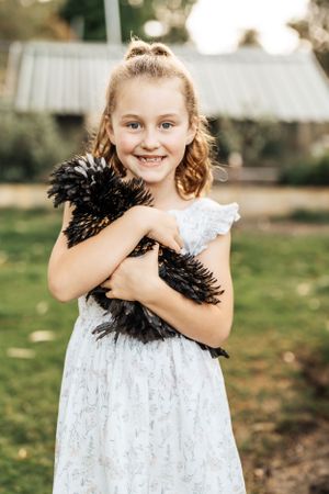 Child in white lace dress holding a black feather boa accessory.