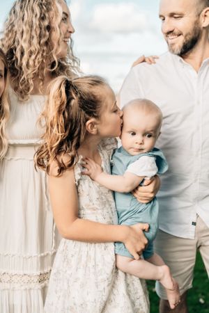 Tender family moment with baby dressed in blue being held and kissed outdoors in soft lighting.