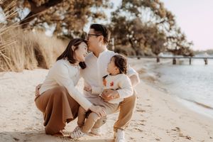 A romantic couple shares tender moments on a sandy beach at sunset in matching neutral outfits.