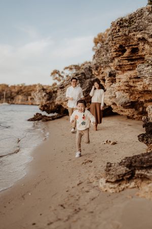 Family enjoying a sunset walk along a scenic rocky beach with dramatic cliffs in the background.