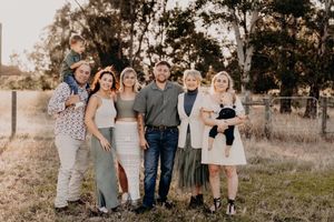 Family group wearing coordinated blue and neutral tones poses together in a rustic outdoor setting at sunset.