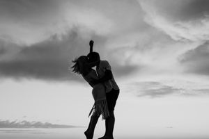 Dramatic black and white silhouette of dancers performing graceful moves against a moody cloudy sky.