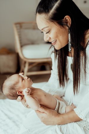 A tender moment between a caregiver and young infant as they share smiles while bonding on white bedding.