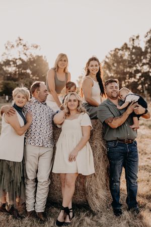 Warm sunset family portrait outdoors with people gathered around hay bale in rustic country setting.