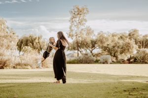 A tender moment captured at sunset with a long black dress silhouette against a warm-lit grassy field and treeline.