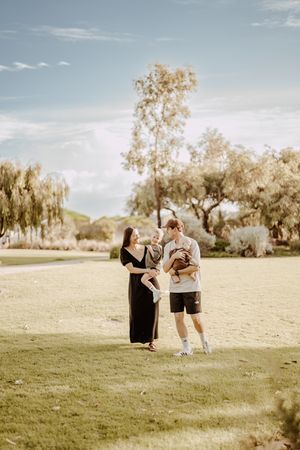 Family photoshoot in an open field with willow trees and mountains in the background.