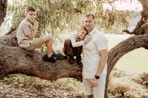 People pose together on a large fallen tree branch during an outdoor golden hour photo session.
