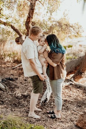 A heartwarming family embraces while standing in a wooded area with autumn leaves in the background.