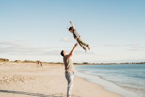 Playful lifting poses on a scenic beach with blue ocean waters.