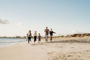 A family running together along a beach shoreline at sunset.